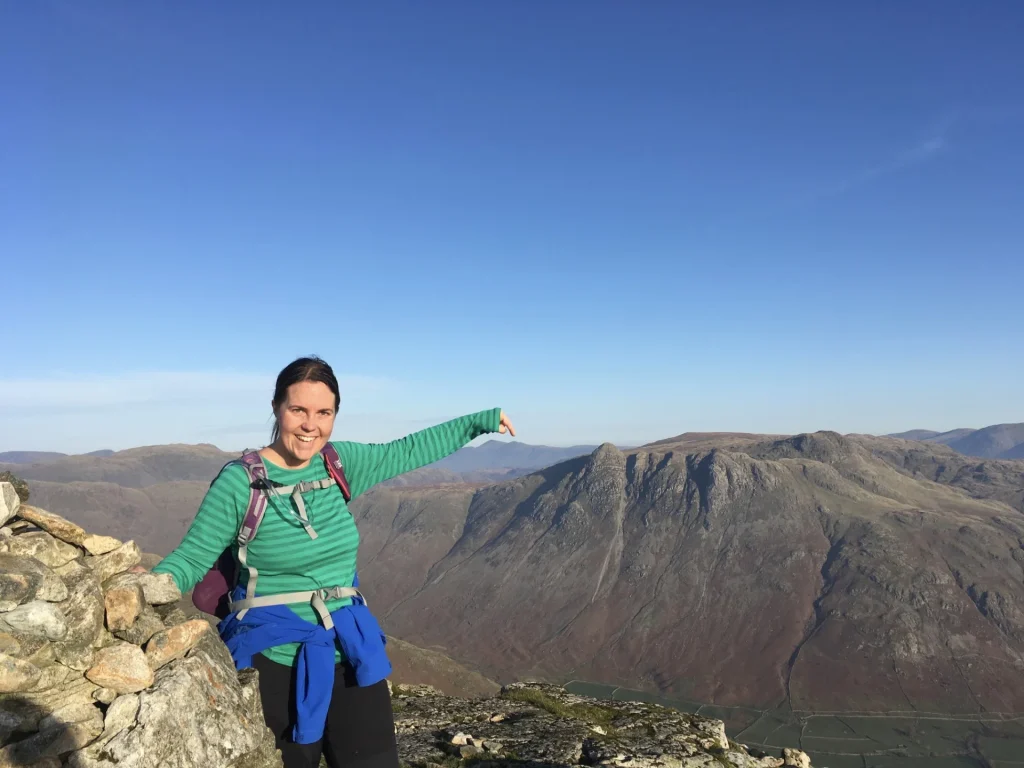 Walker on a Lake District fell pointing down toward the valley