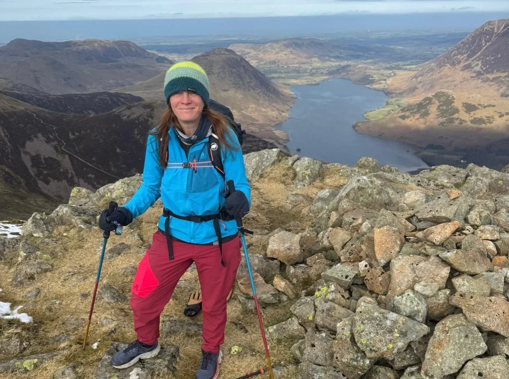 Ros standing with walking poles on a rocky summit above Ennerdale Water on the North Ennerdale Skyline