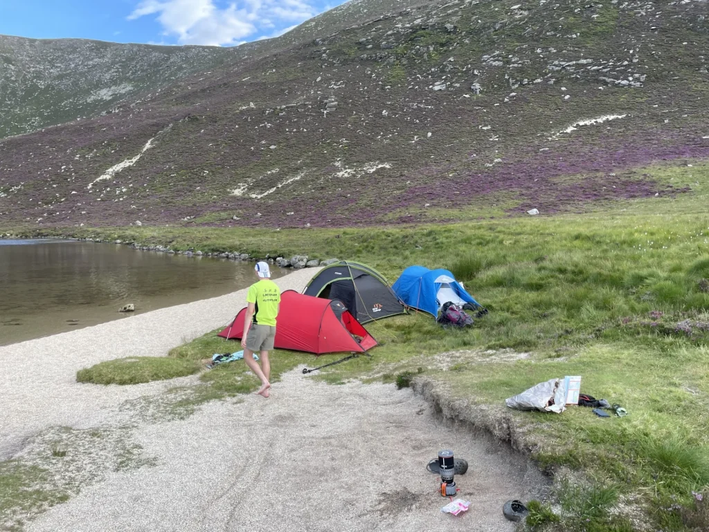 Wild camping tents beside a Lake District tarn with hills in the background